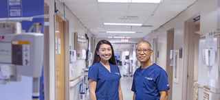 Two nurses in blue scrubs stand in a clinical hallway
