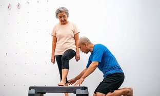 Woman doing step-ups with male trainer kneeling beside her