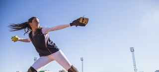 Woman in softball uniform throwing a softball