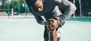 Man on green court stretching leg
