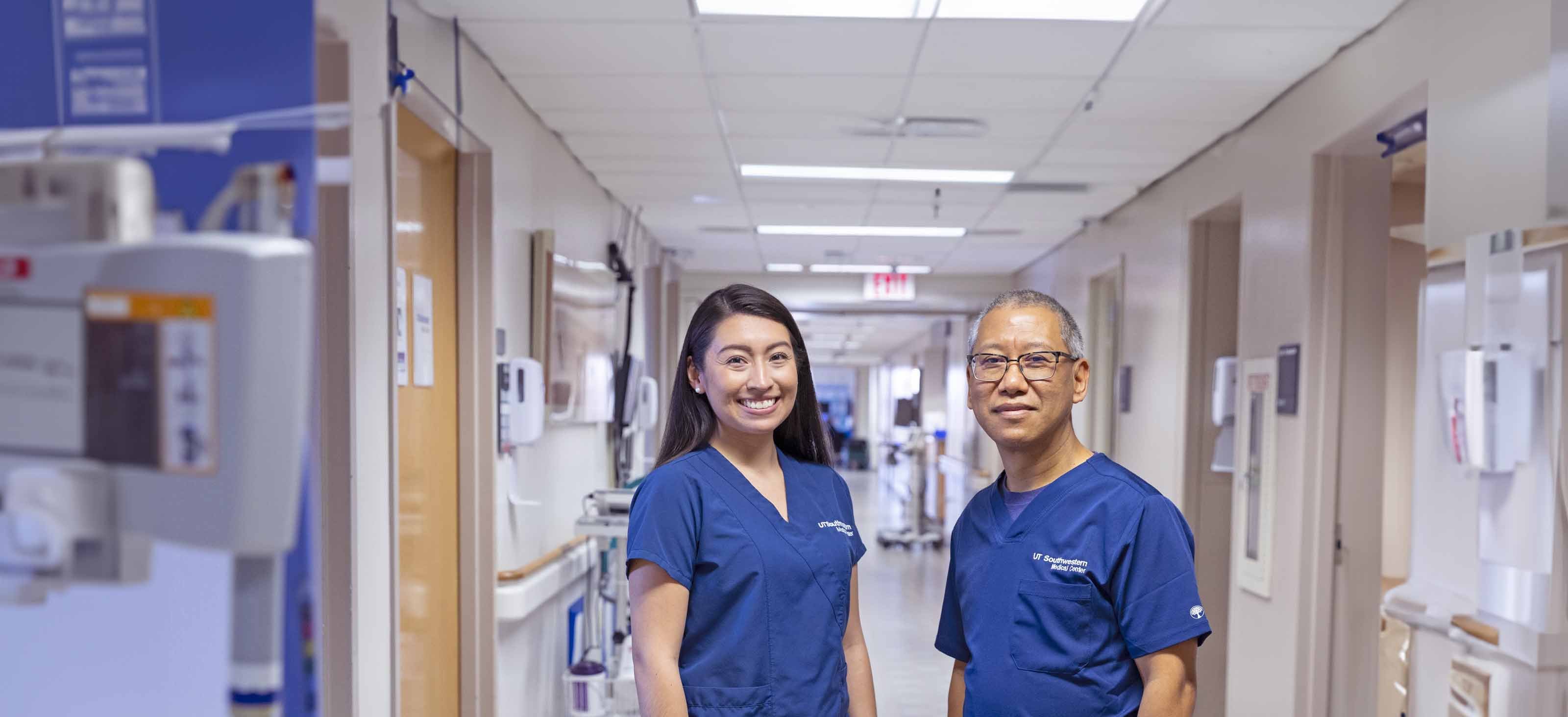 Two nurses in blue scrubs stand in a clinical hallway