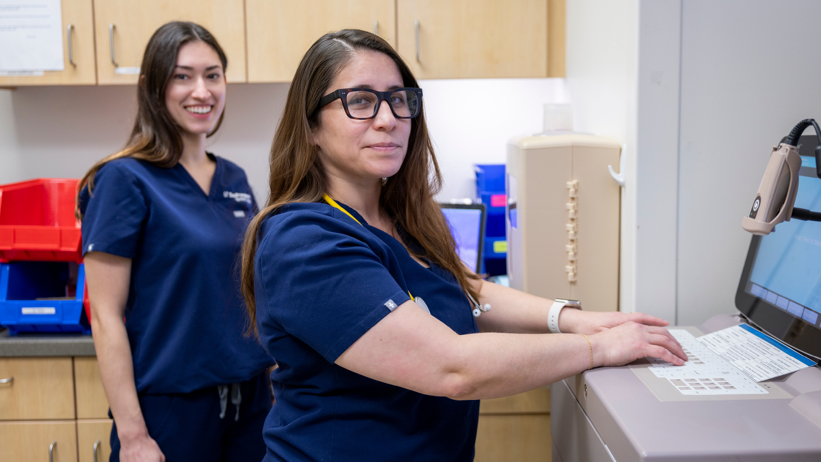 Two nurses working on computer while looking to camera.