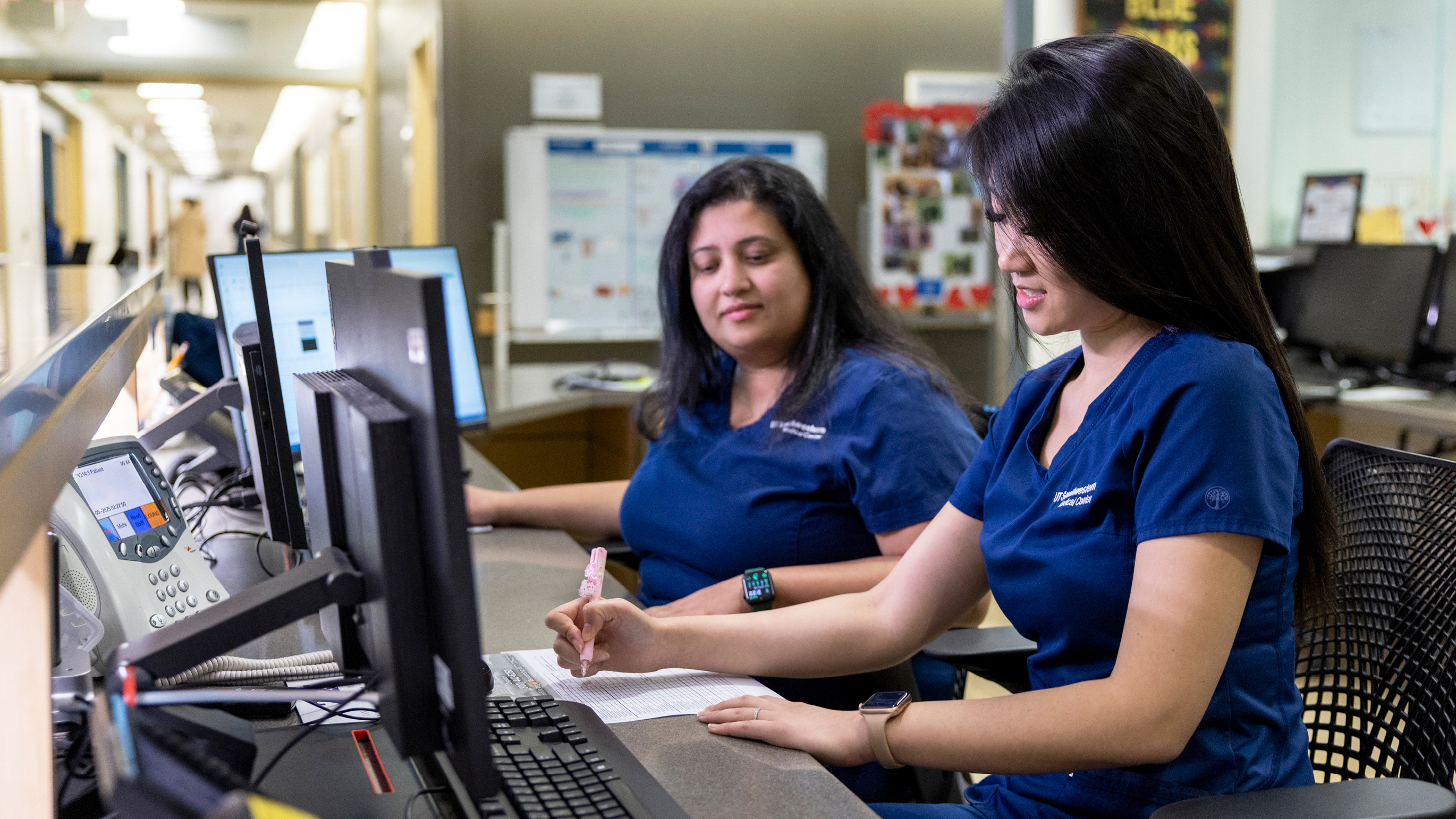 two nurses working at a station in front of a computer.