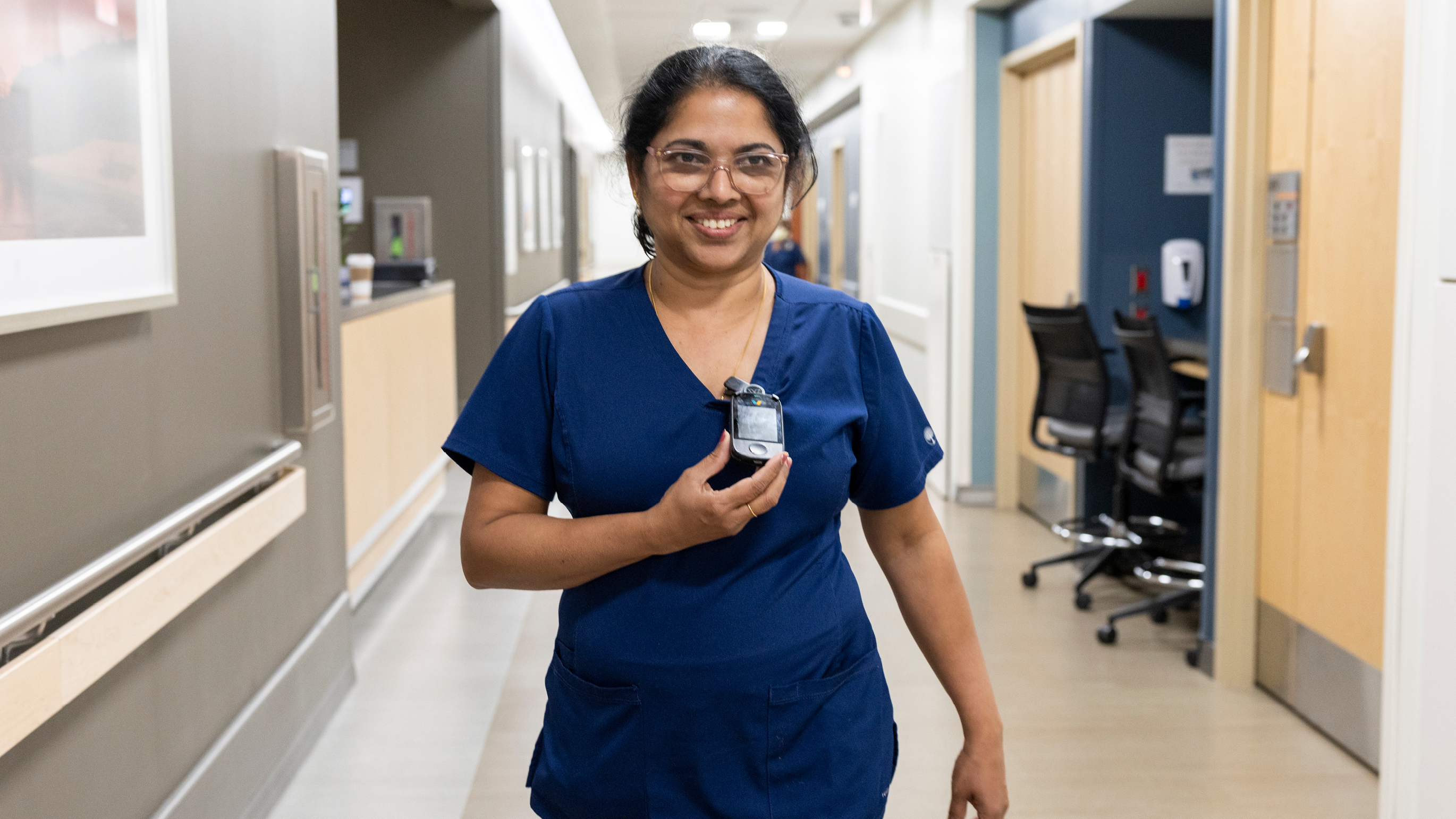 Nurse walking through halls and holding her Vocera device.