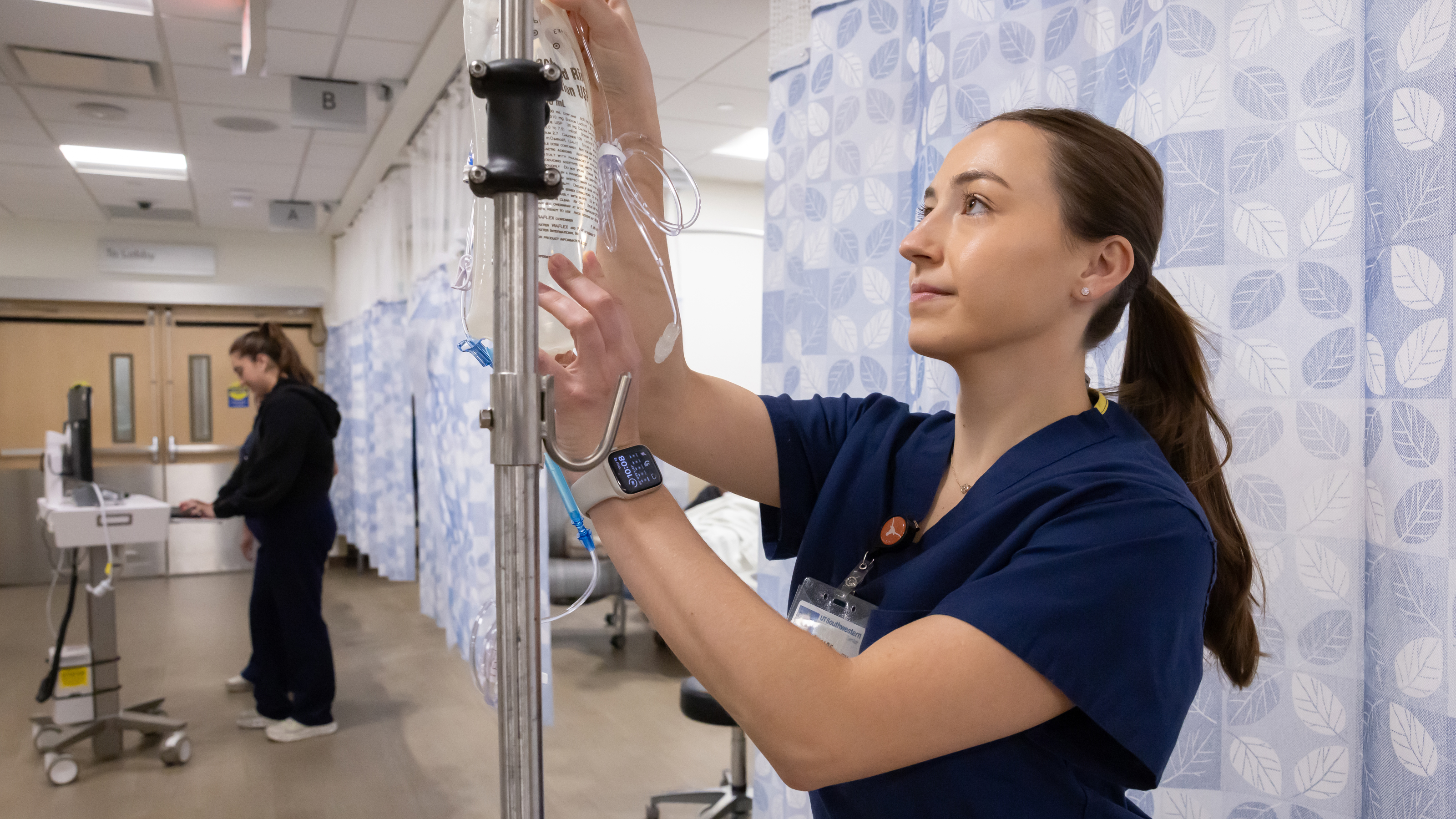 A female nurse in a ponytail measures fluid in an IV bag