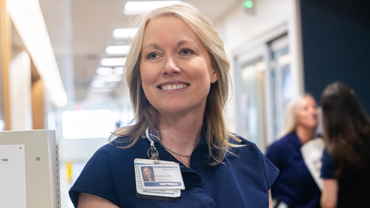 A female nurse in blue scrubs smiling at someone off camera.