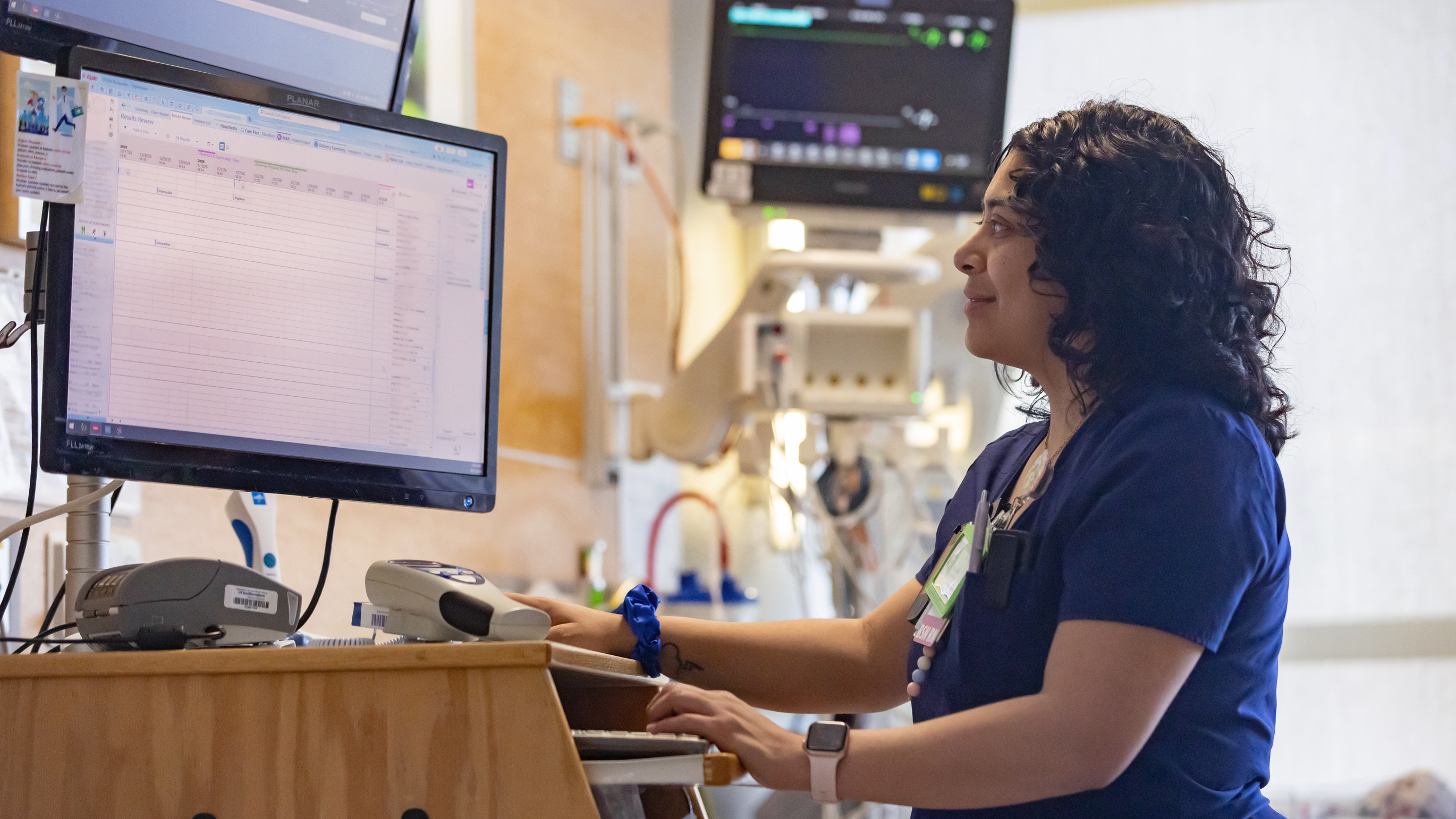 A nurse standing at a computer next to a patient bed.