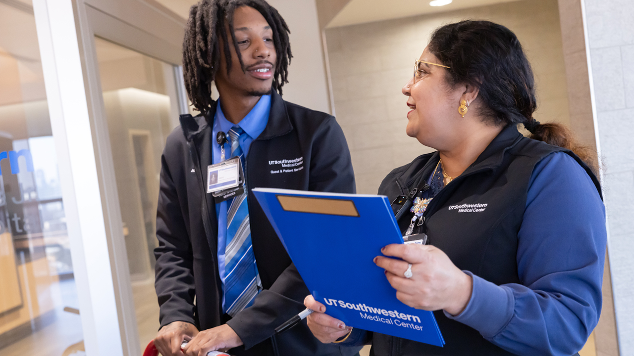 Two nurses having a discussion. One is holding a blue folder that says UT Southwestern Medical Center.
