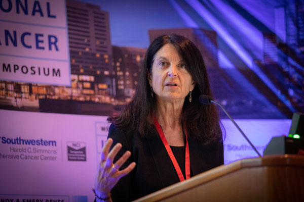 Speaker presenting at a podium during a breast cancer symposium