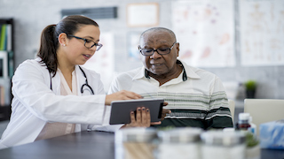 A doctor shows an elderly patient information on a tablet during a consultation in a medical office
