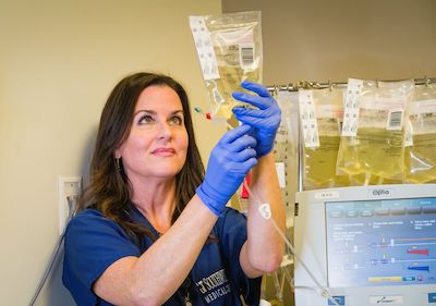 A nurse with a bag of blood in hand, standing in front of a computer.