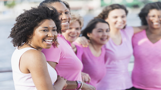 A group of women, all wearing pink shirts, smile and stand close together, supporting each other in a show of unity