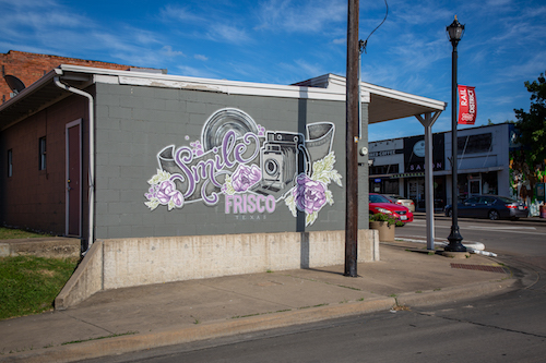 A street corner featuring a "Frisco Smile" mural on a gray wall.