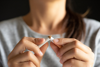 A woman breaks a cigarette in half with her hands, symbolizing quitting smoking