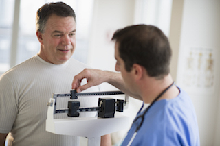 A man stands next to a doctor as he weighs himself