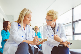 Two female doctors in white coats discussing medical notes