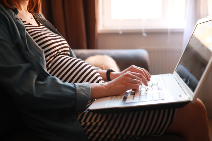 A pregnant woman sits with a laptop