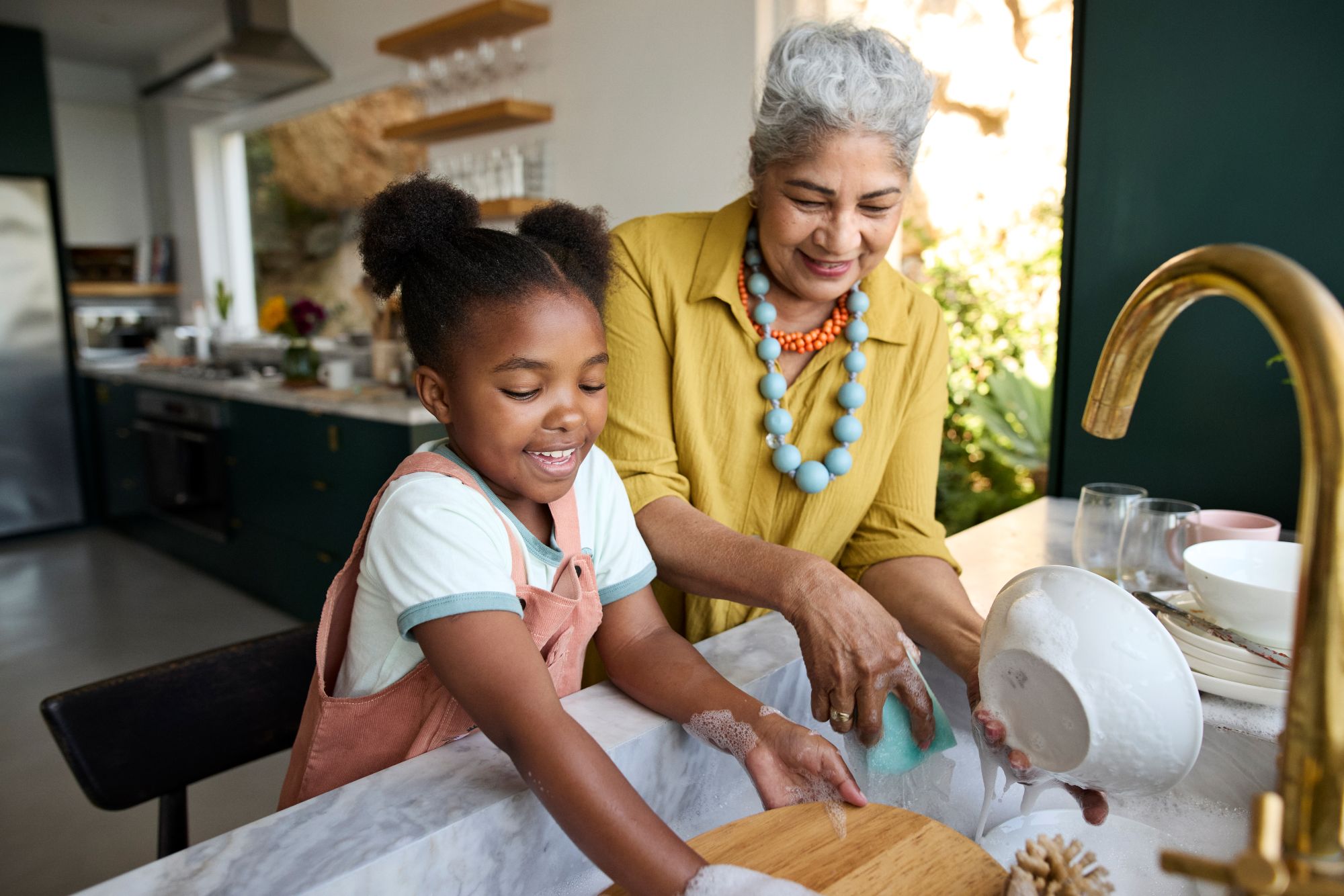 Young girl helping her grandmother wash dishes in the kitchen.