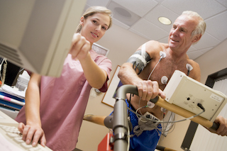 Older male patient undergoing a stress test on a treadmill, monitored by a healthcare professional