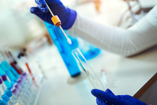 A scientist wearing gloves uses a pipette to transfer a liquid into a test tube in a laboratory