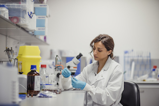 A scientist in a laboratory coat carefully examines a sample using a pipette while surrounded by various lab equipment