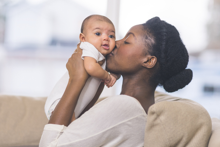 A mother lifts her baby and kisses its face