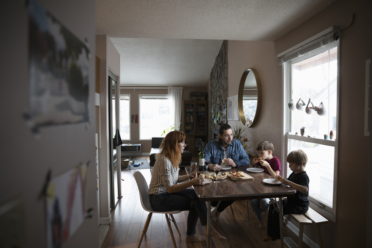 A family of four sits around a dining table in a cozy, well-lit home, enjoying a meal together