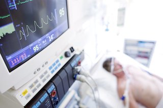 Patient being monitored in a hospital bed, with a close-up of a medical monitor displaying vital signs