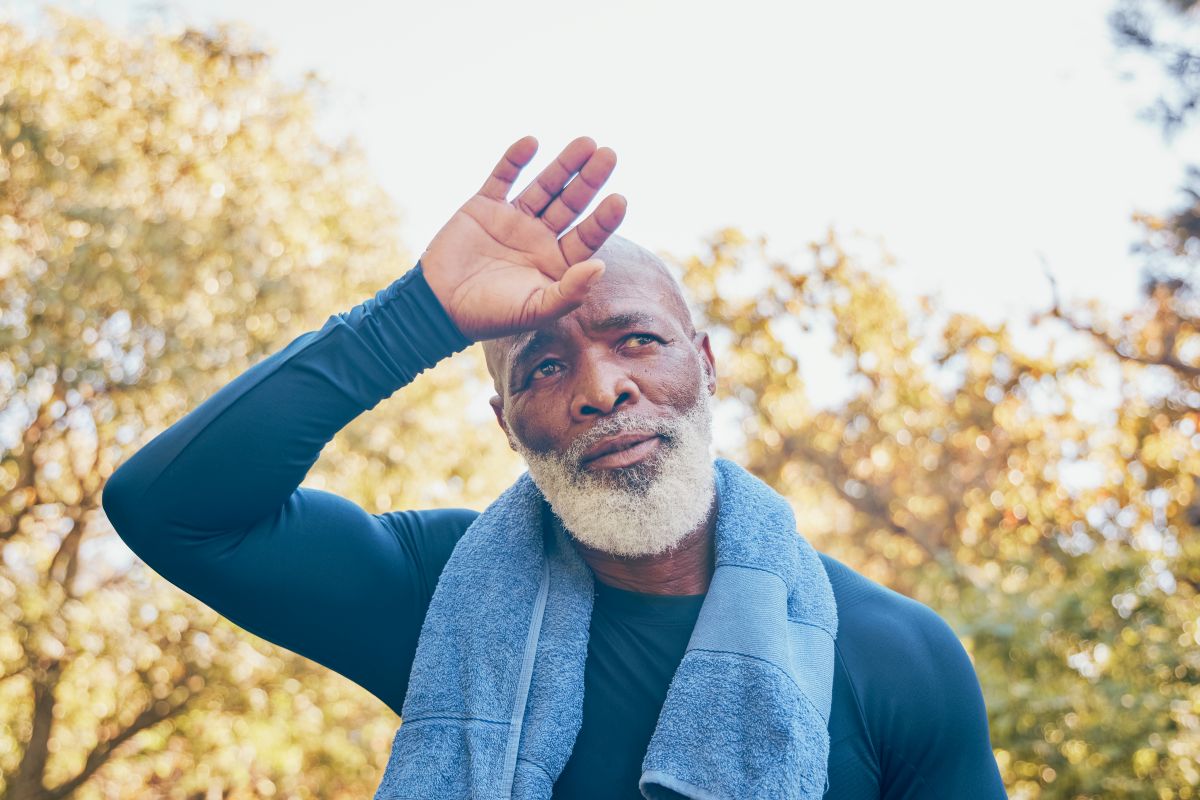 Older man wipes his forehead in the heat after exercising outside.
