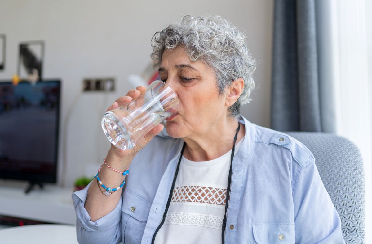 An elderly woman drinks water at home.