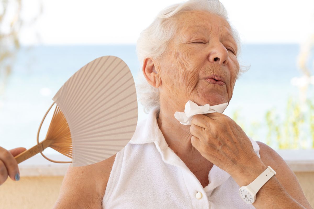 Older adult woman trying to cool off with fan in the heat.