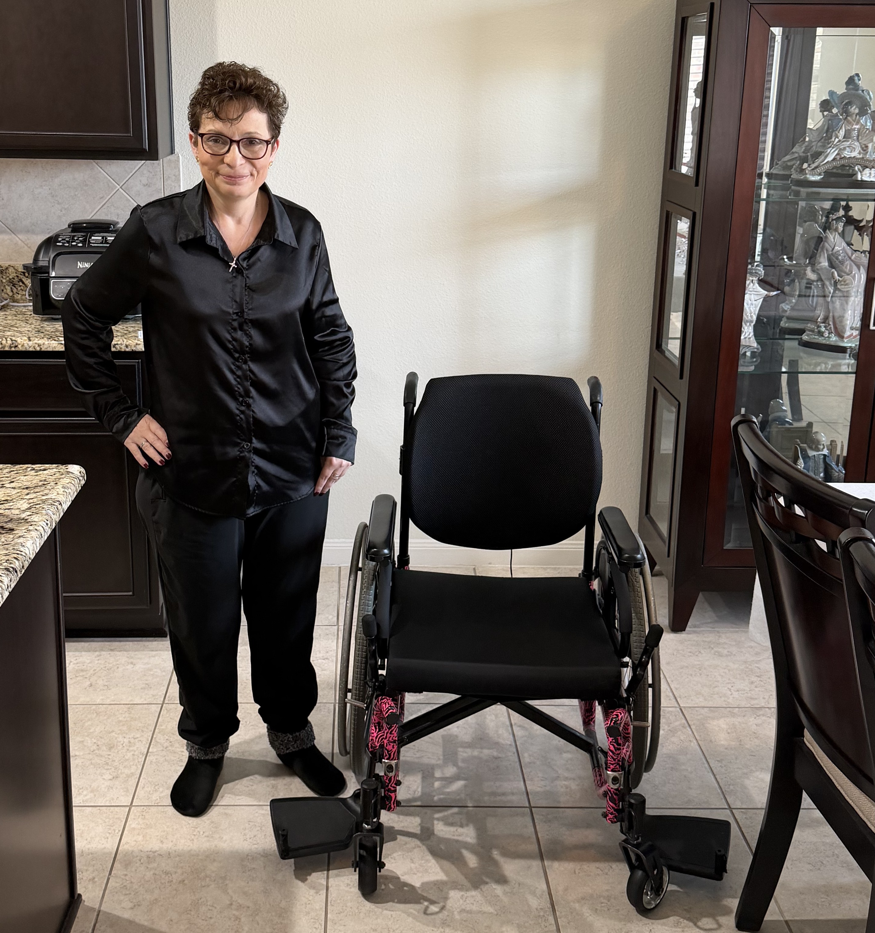 Patient Paige Montgomery standing next to wheelchair at home