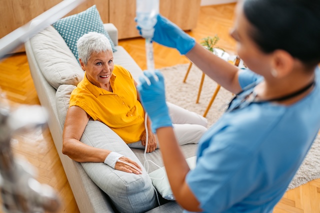 Home Care Nurse Adjusting IV Drip On A Senior Woman While Visiting Her At Her Home