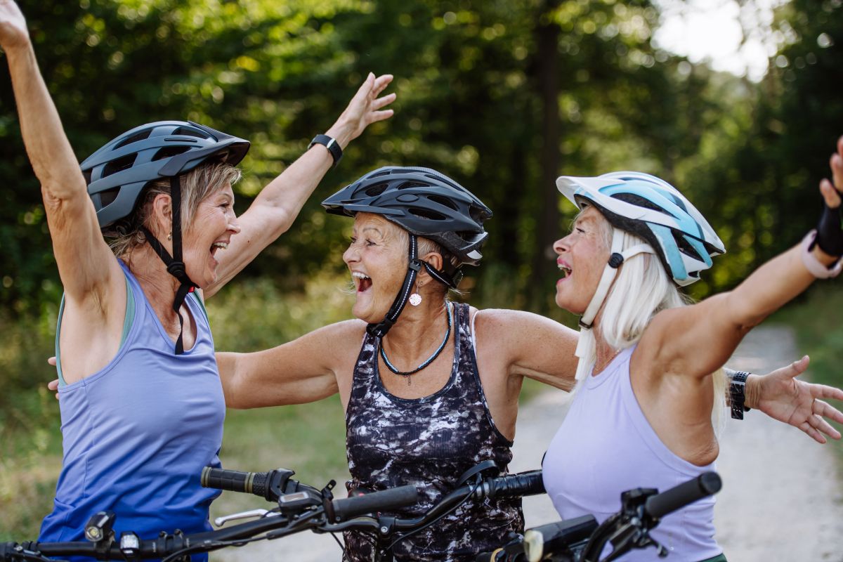 Three elderly women celebrate during a bike ride in nature.