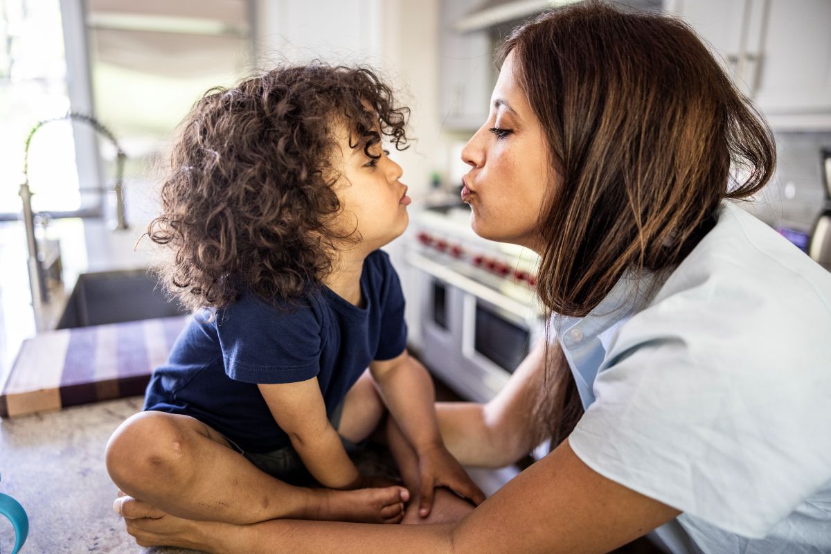 A mother kisses her toddler son in the kitchen of their home.