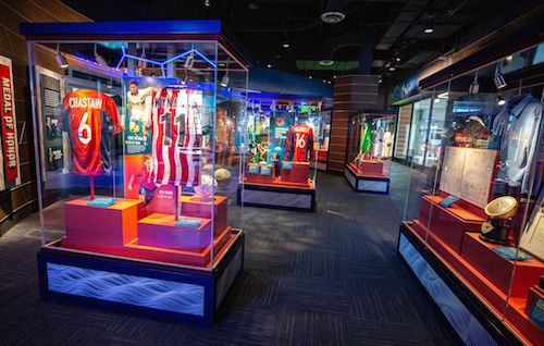 An indoor exhibit at the National Soccer Hall of Fame featuring sports memorabilia, including jerseys and trophies, with bright, colorful displays.