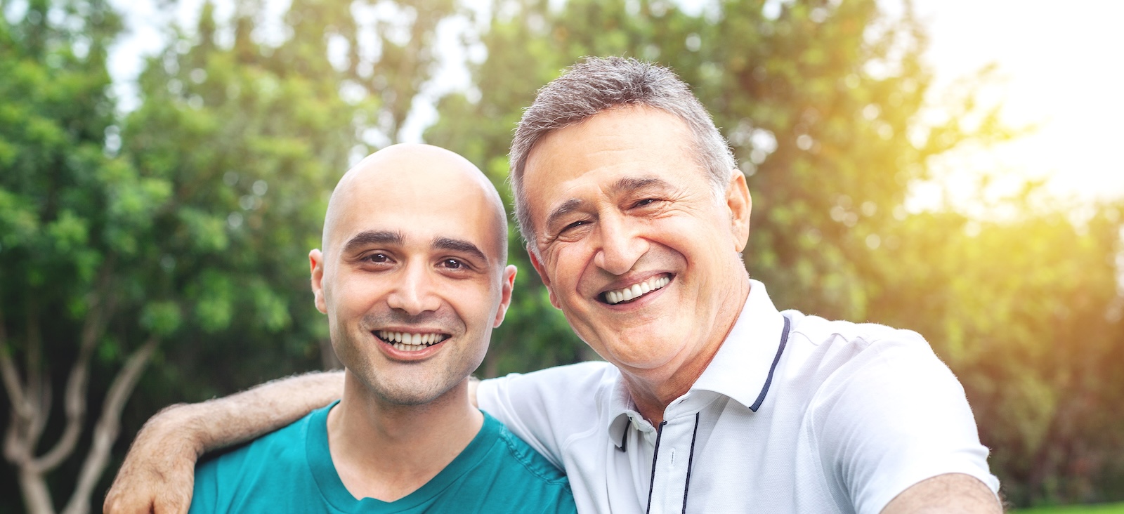 A young man with a shave head and an older man, smiling