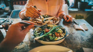 Two people enjoy a meal together at a rustic table, with a bowl of fresh salad and various dishes being shared