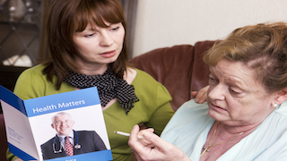 A concerned woman talks with an elderly woman, who is holding a cigarette and looking at a brochure about quitting smoking