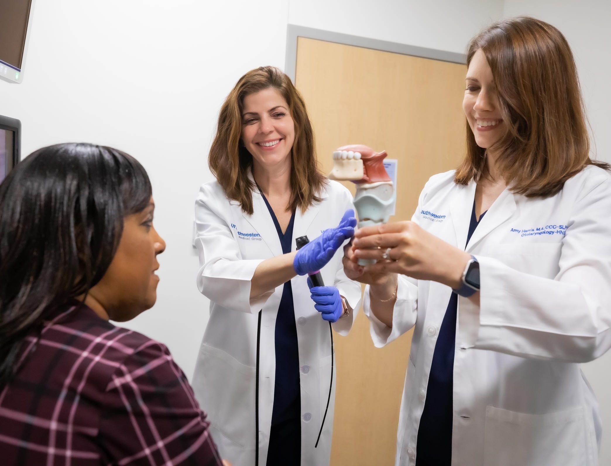 This image shows a patient and two healthcare providers in a clinical setting, illustrating a voice care session or vocal therapy.