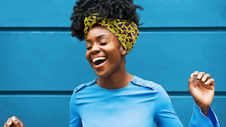 A woman smiling widely with her arms raised, possibly singing.