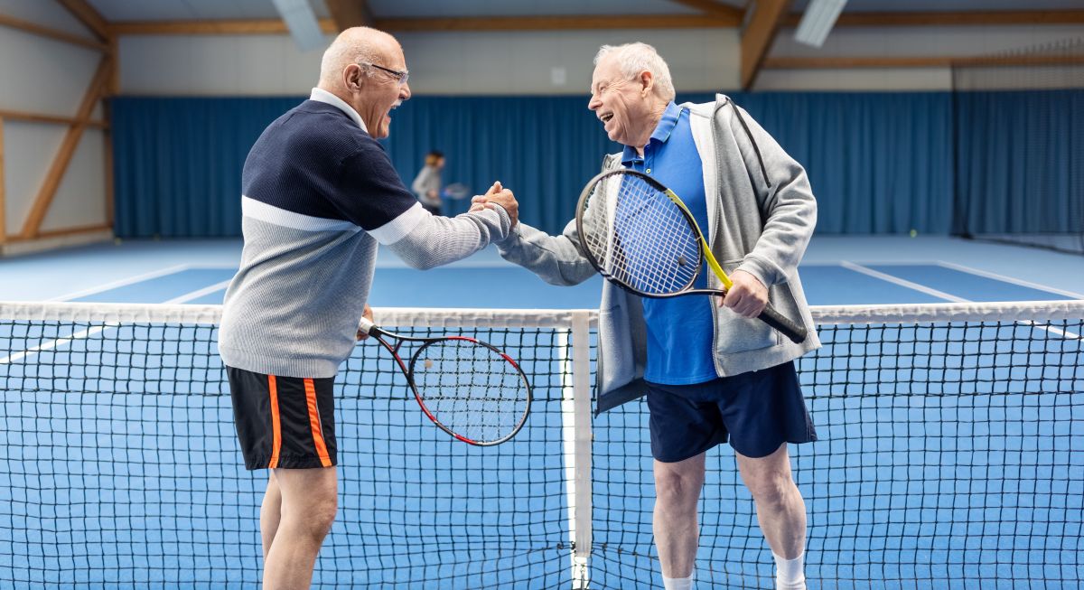 Two senior citizens shake hands after a tennis game.