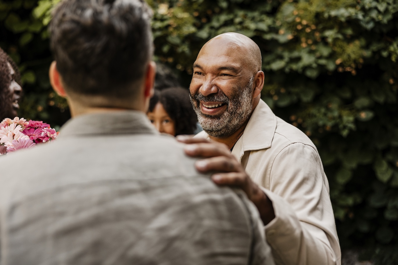 Happy African American senior man with hand on shoulder of male friend at dinner party