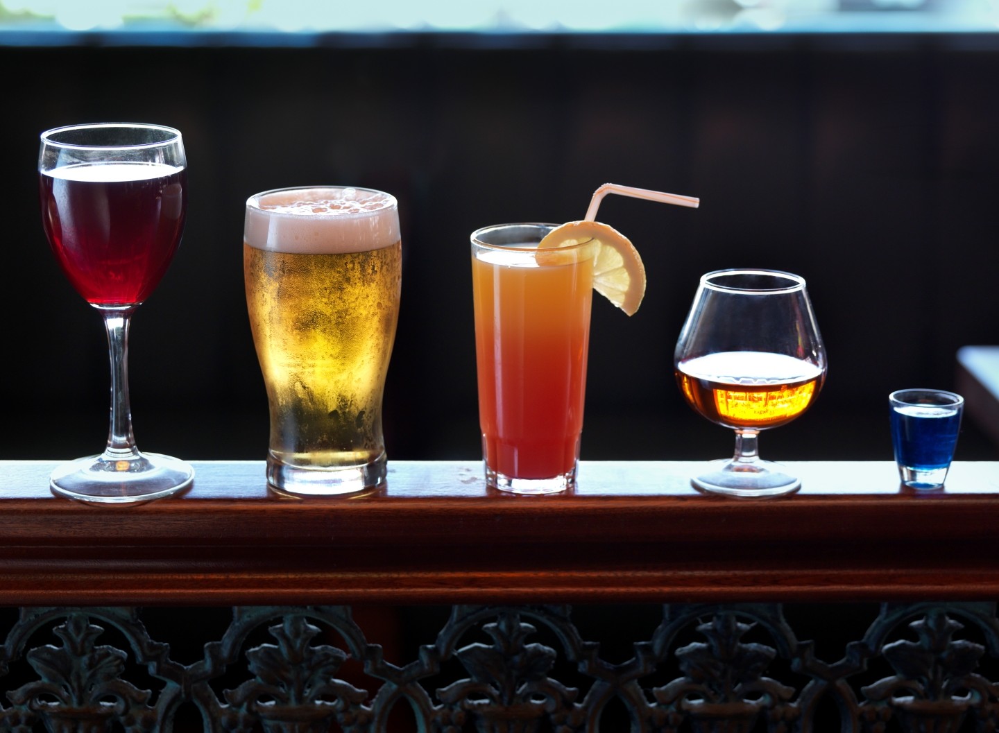 Various alcoholic drinks - wine, beer, mixed drink, liquor - lined up in serving sizes on bar rail