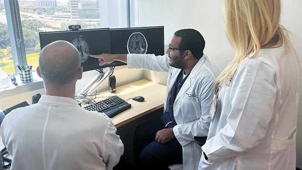 Three doctors in lab coats examining a computer screen