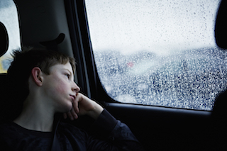 Boy looking out the car window on a rainy day