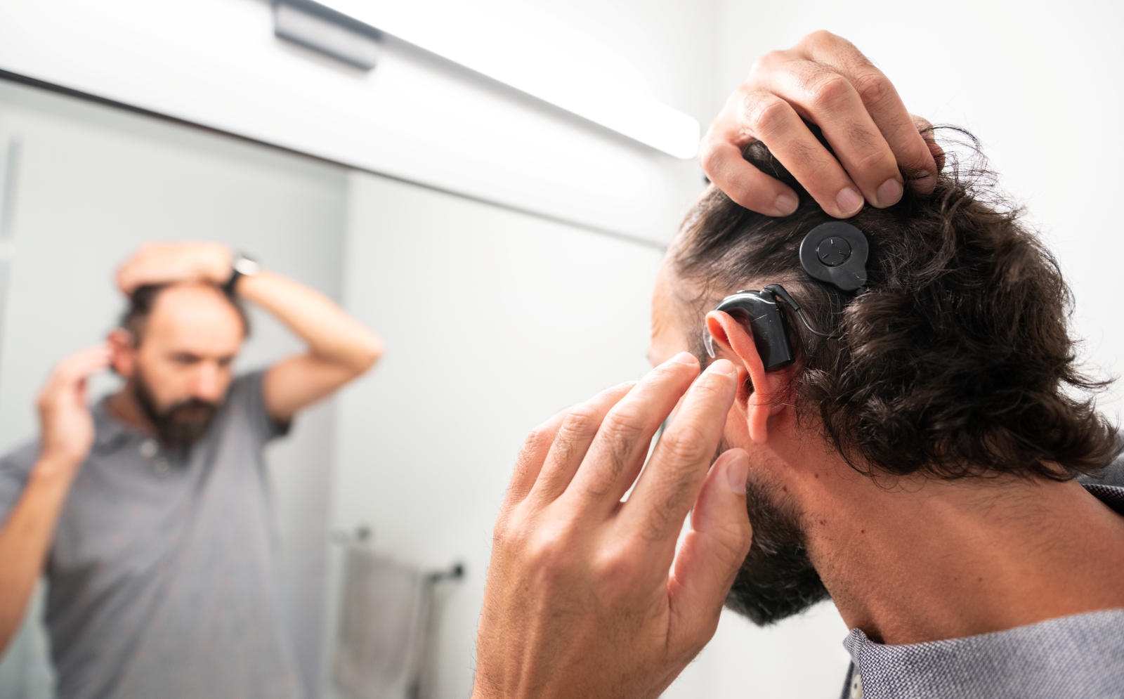 Man adjusts cochlear implant while looking into mirror