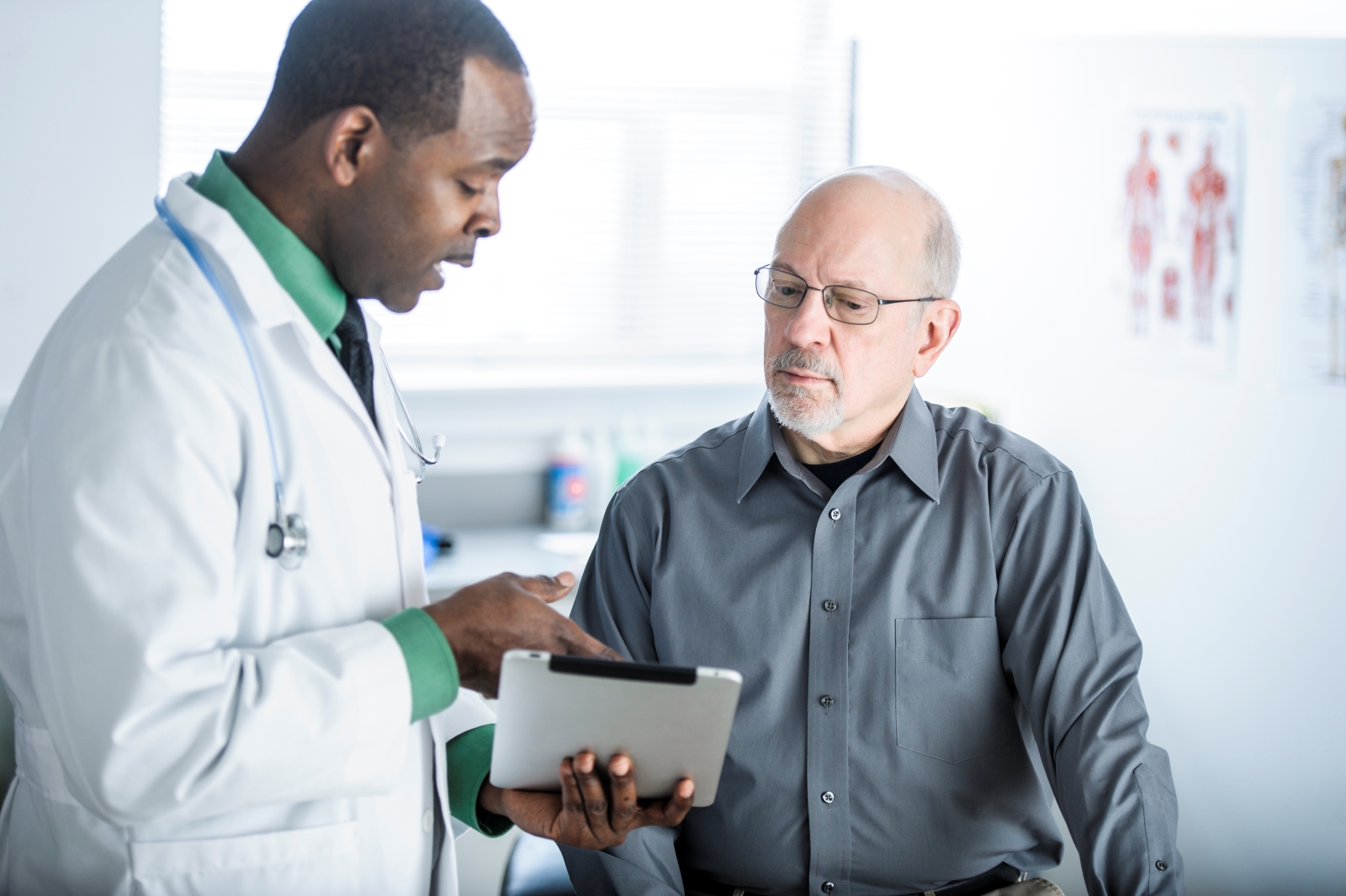 doctor talking with male patient and explaining something on tablet