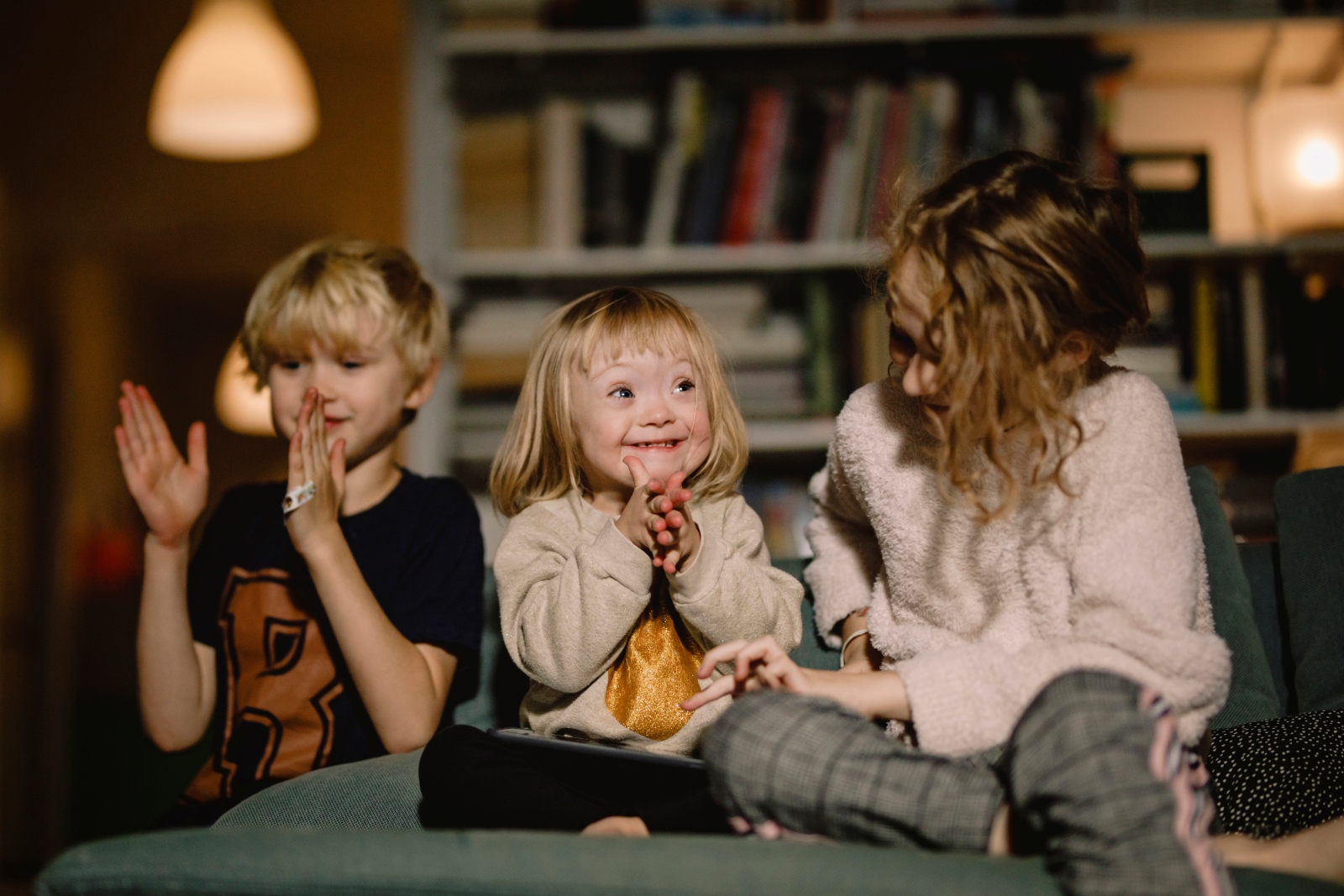 A young girl with Down syndrome is clapping while sitting between a boy and an older girl.