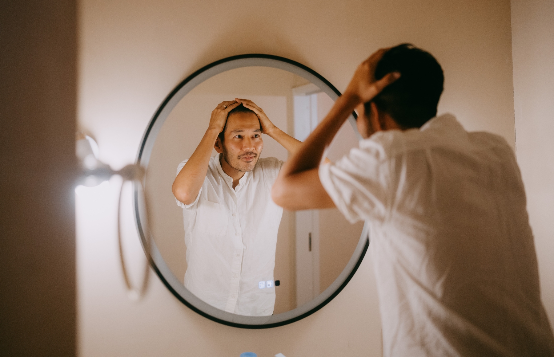 Man looking at self in circular mirror hanging on wall and feeling distressed.
